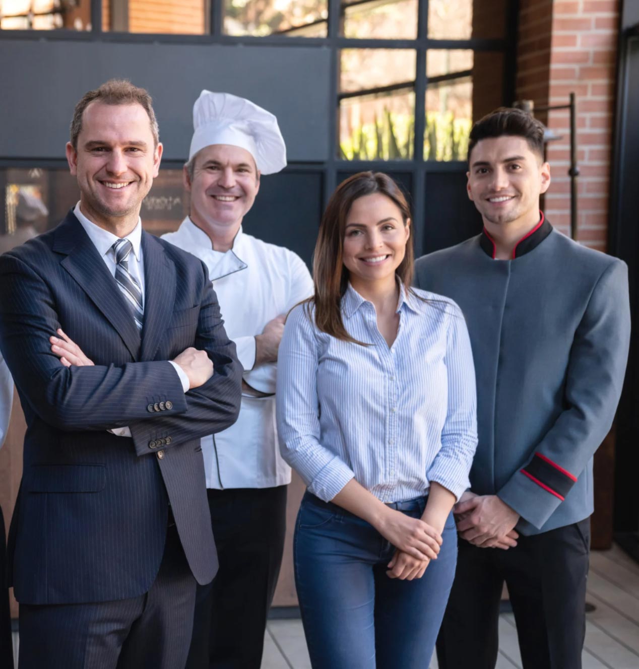 Four smiling professionals, including a chef, stand together in front of a modern restaurant entrance.